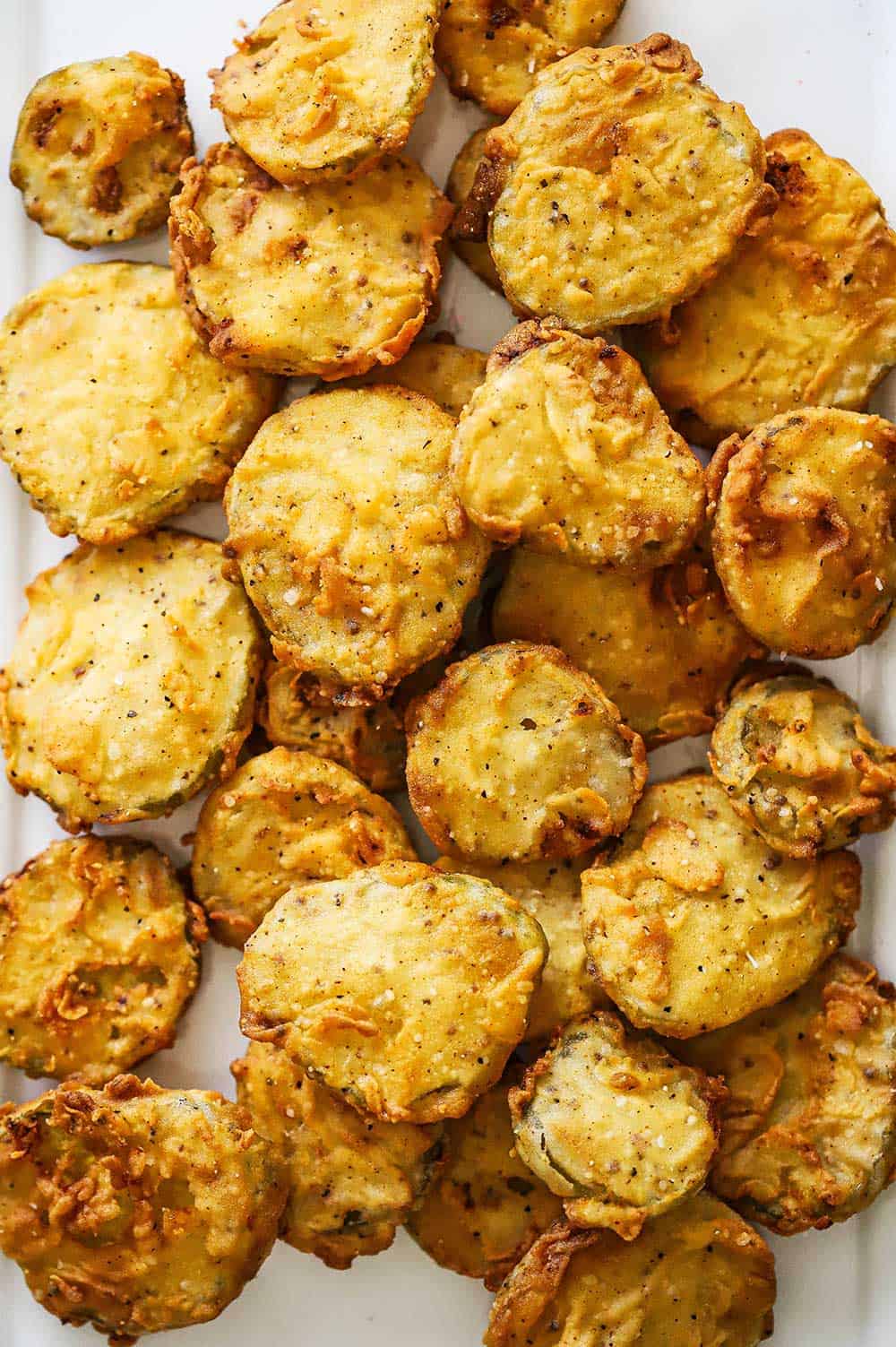 A white oval platter filled with golden brown fried pickles.