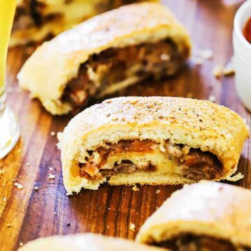 A line up of sliced sausage bread sitting on a wooden cutting board next to a glass of beer.