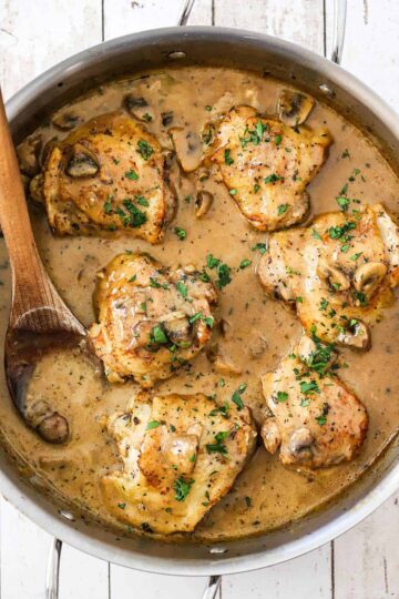 An overhead view of a stainless steel skillet filled with six pieces of chicken fricassee with a creamy mushroom sauce.