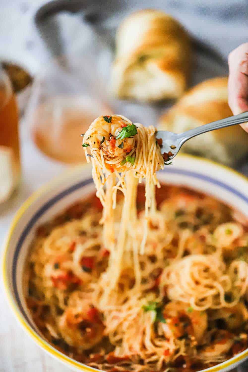 A person lifting up a fork that has pasta wrapped with cooked shrimp marina and angel hair pasta.