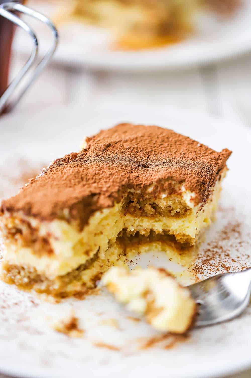 A plate of tiramisu with a bite taken out of it on a nearby fork.