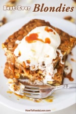 A white dessert plate filled with two blondies stacked on top of each other with a partially melted scoop of vanilla ice cream on top with a fork sitting next to it.