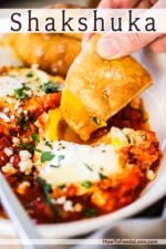 A person dipping a toasted pita triangle into a poached egg nestled into shakshuka.