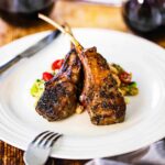 Two marinated grill lamb chops on sitting on a Greek salad on a white dinner plate.