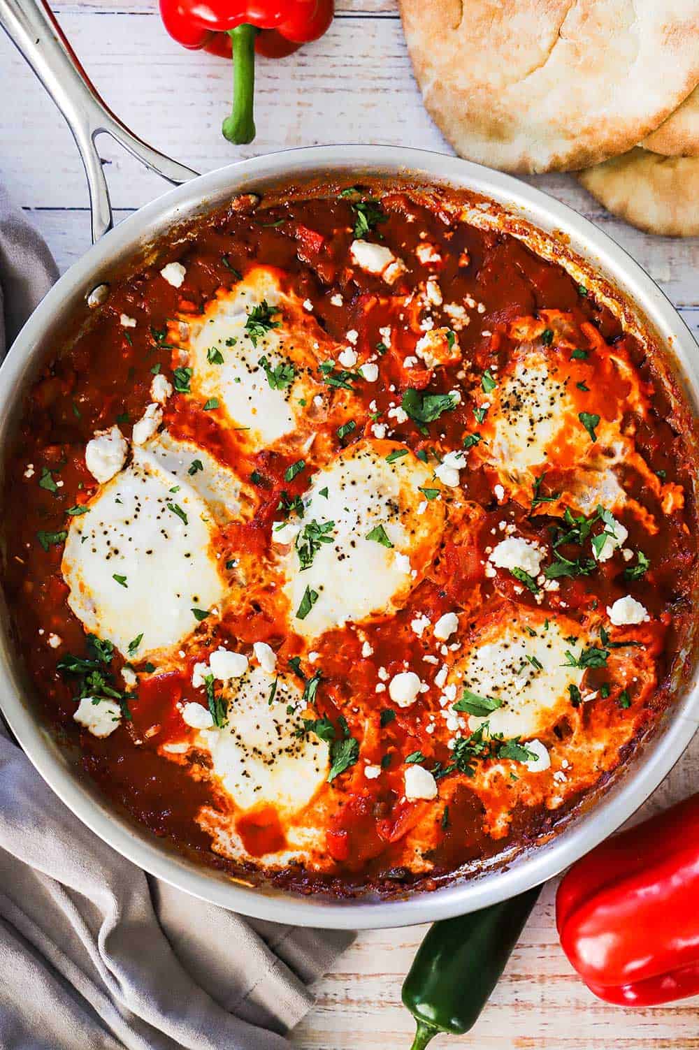 An overhead view of a large stainless steel skillet filled with poached eggs in a vibrant red tomato sauce.