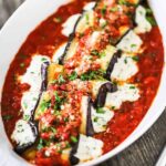 A close up view of baked eggplant rollatini with cheese oozing out the sides of each roll all nestled in a bed of marinara sauce.