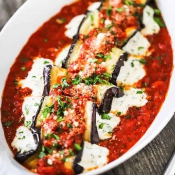 A close up view of baked eggplant rollatini with cheese oozing out the sides of each roll all nestled in a bed of marinara sauce.