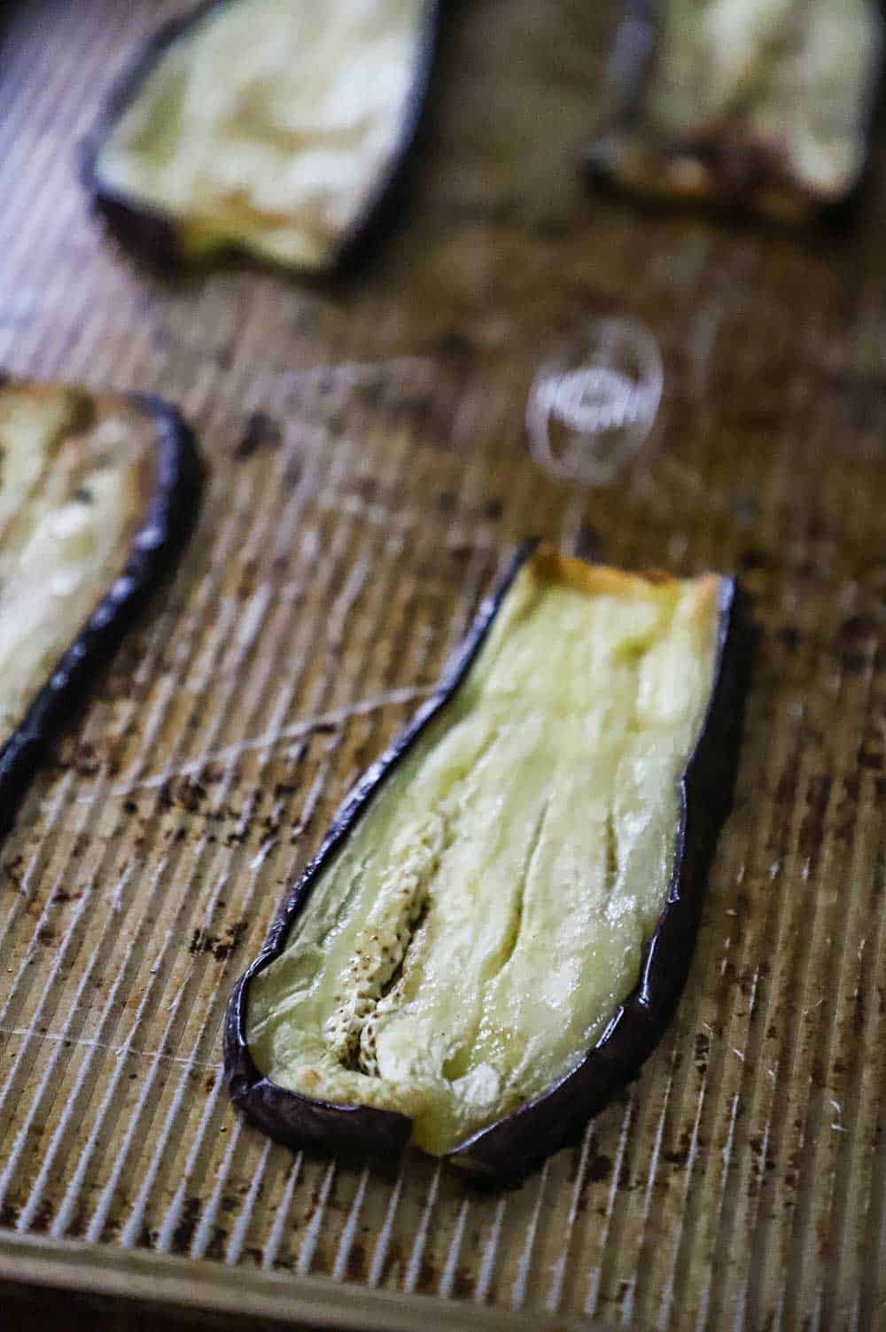 Several strips of eggplant that have been roasted on a large baking sheet.