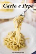 A person using a fork to lift up a helping of cacio e pepe from a white dinner plate.