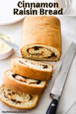 A loaf of cinnamon raisin bread that has three slices cut and are sitting on parchment pater next to a serrated knife and a bowl of softened butter.