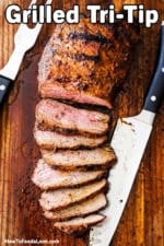 A sliced grilled tri-tip steak on a cutting board with a large knife next to it.