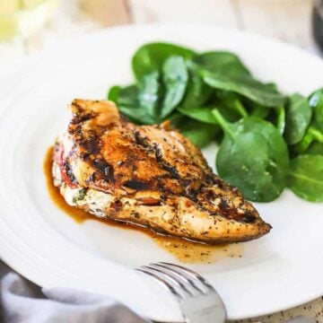A white dinner plate filled with a caprese-stuffed chicken breast and topped with a balsamic glaze.