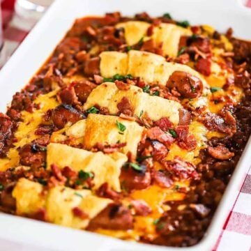 A chili cheese dog casserole topped with crumbled bacon in a white baking dish.
