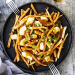 An overhead view of a black dinner plate filled with poutine with two forks on each side.