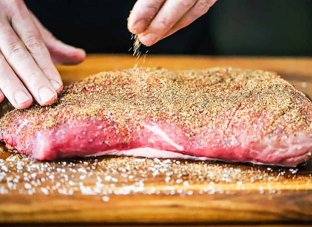 A person sprinkling a beef run all over an uncooked tri-tip steak.