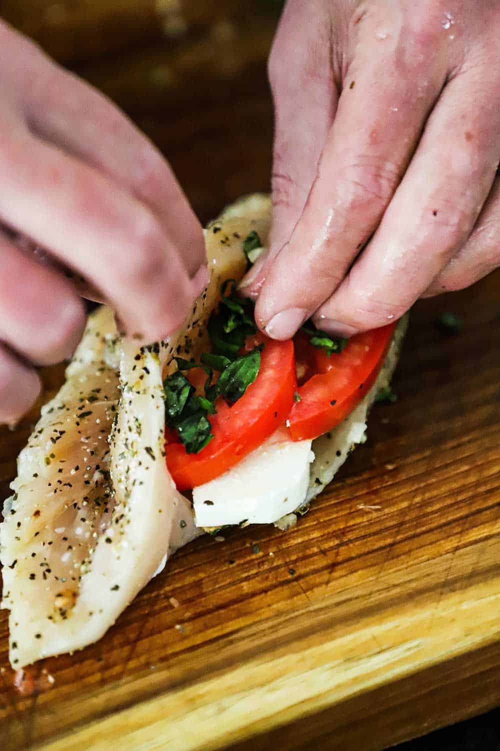 A person stuffing a chicken breast with slices of mozzarella, tomatoes, and basil.