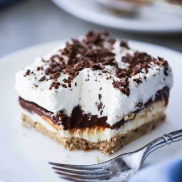 A square serving of layered chocolate delight sitting on a white plate with a bite missing.