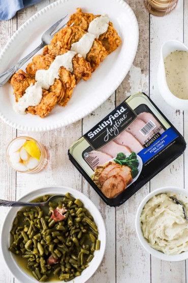 An overhead view of a package of Smithfield boneless pork chops next to a platter filled with five Southern-fried pork chops topped with cream gravy.