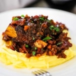 A plate of mashed potatoes topped with braised beef short ribs and a tomato vegetable sauce.