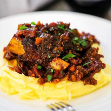 A plate of mashed potatoes topped with braised beef short ribs and a tomato vegetable sauce.