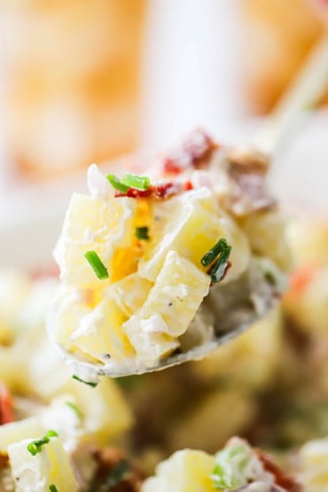 A large spoon holding up a heaping pile of creamy horseradish potato salad.