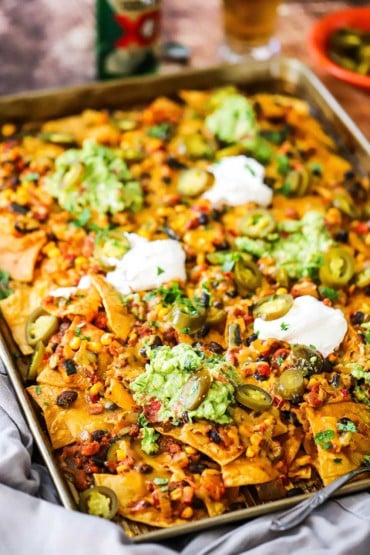A straight-on view of sheet pan nachos topped with dollops of guacamole and sour cream.