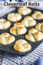 A muffin pan filled with freshly baked cloverleaf dinner rolls sitting on a wire baking rack.