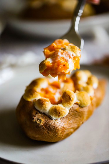 A person using a fork to lift up the filling from a twice baked sweet potato that is topped with lightly browned marshmallows.