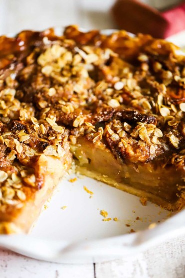 An apple pie with caramel in a white pie dish with a large piece missing.
