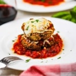Air fryer eggplant parmesan that is two stacked breaded and fried eggplant circles topped with cheese and on a small pool of marinara sauce on a white plate.