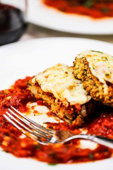 A plate of air fryer eggplant parmesan with a bite taken out of it with the fork on the plate.