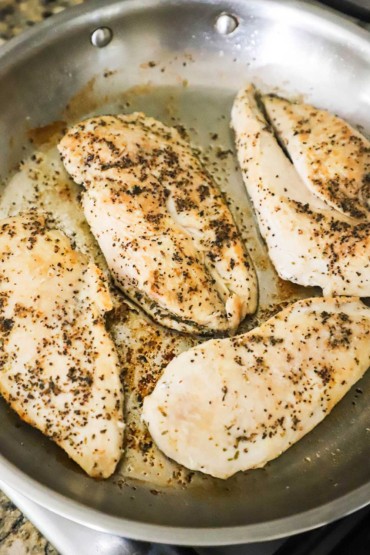 A silver skillet filled with four seasoned boneless chicken breasts that have been seared in olive oil