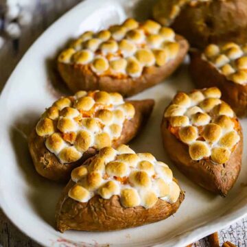 A large oval platter holding five twice baked sweet potatoes that are topped with toasted marshmallows