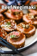 A close-up view of slices of beef negimaki on a platter topped with a brown sauce and sesame seeds.