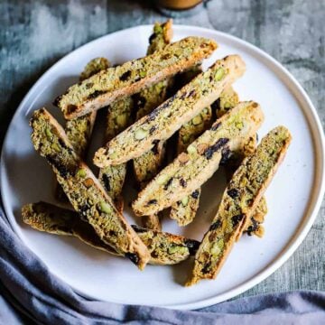 An overhead view of a white plate filled with a stack of pistachio and dried cherries biscotti.
