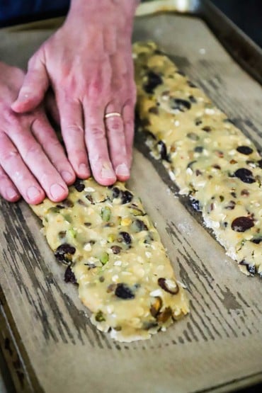 A pair of hands pressing on a flattened rectangular piece of biscotti dough on a baking pan.