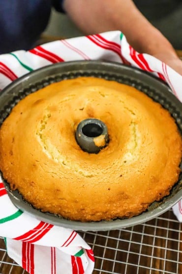 A person holding a bundt pan filled with a baked gold cake.