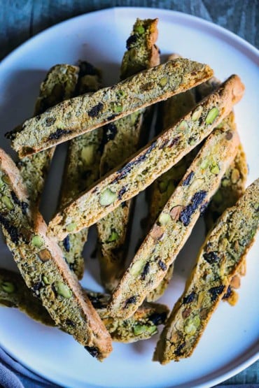 An overhead view of a white plate filled with a stack of pistachio and dried cherries biscotti.