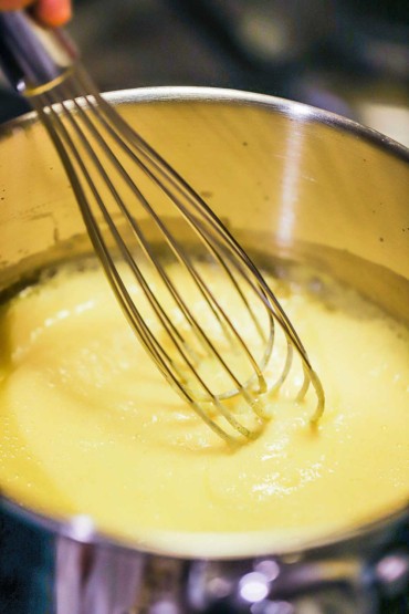 A stainless steel saucepan filled with an egg yolk foam sauce with a whisk in the middle.