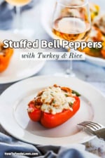 A single turkey and rice stuffed bell pepper sitting on a white plate next to a glass of wine.