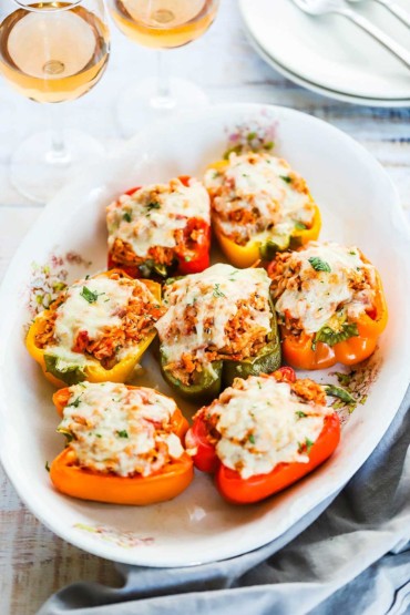 A large oval antique platter that is filled with turkey and rice stuffed bell peppers sitting next to glasses of wine.