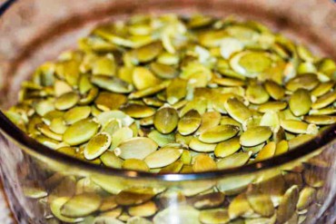 A small glass bowl filled with green pumpkin seeds.