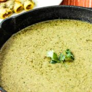 A black cast-iron skillet filled with pumpkin seed (Pipián) sauce with a sprig of cilantro in the middle.