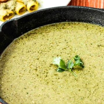 A black cast-iron skillet filled with pumpkin seed (Pipián) sauce with a sprig of cilantro in the middle.