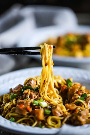 A pair of chopsticks lifting noodles up from a bowl of slow-cooker chicken chow mein.