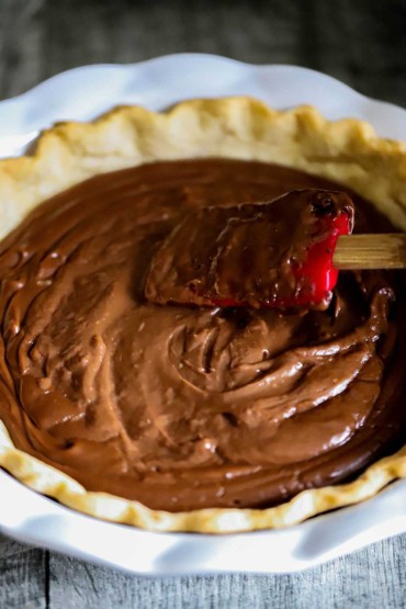 A spatula being used to smooth the top of a pie that is filled with chocolate cream in a homemade crust.