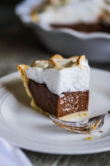 A slice of chocolate meringue pie on a dessert plate with a fork nearby and a bite missing from the piece.