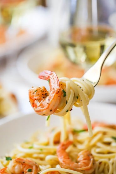 A fork being used to hold up cooked pasta that is twirled on the utensil with a sautéed shrimp also attached.