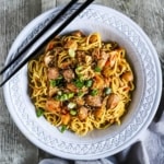 An overhead view of a grey bowl filled with slow-cooker chicken chow mein flanked by two black chopsticks.