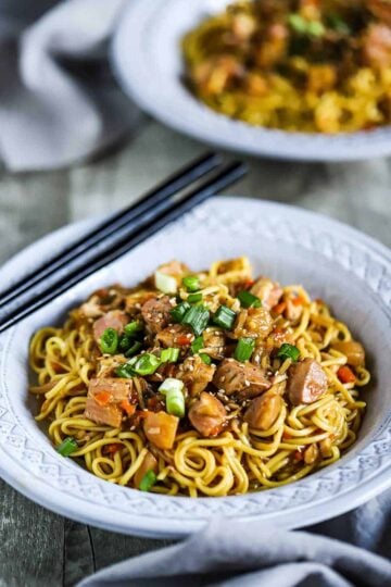 Two bowls filled with slow-cooker chicken chow mein with the bowl in the forefront holding two chopsticks on the side.